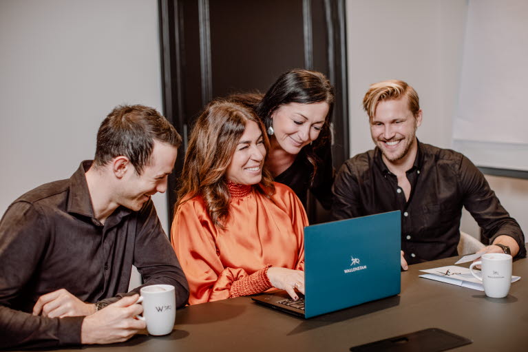 Två kvinnor och två män sitter framför en laptop med Wallenstamloggan. De pratar och skrattar.