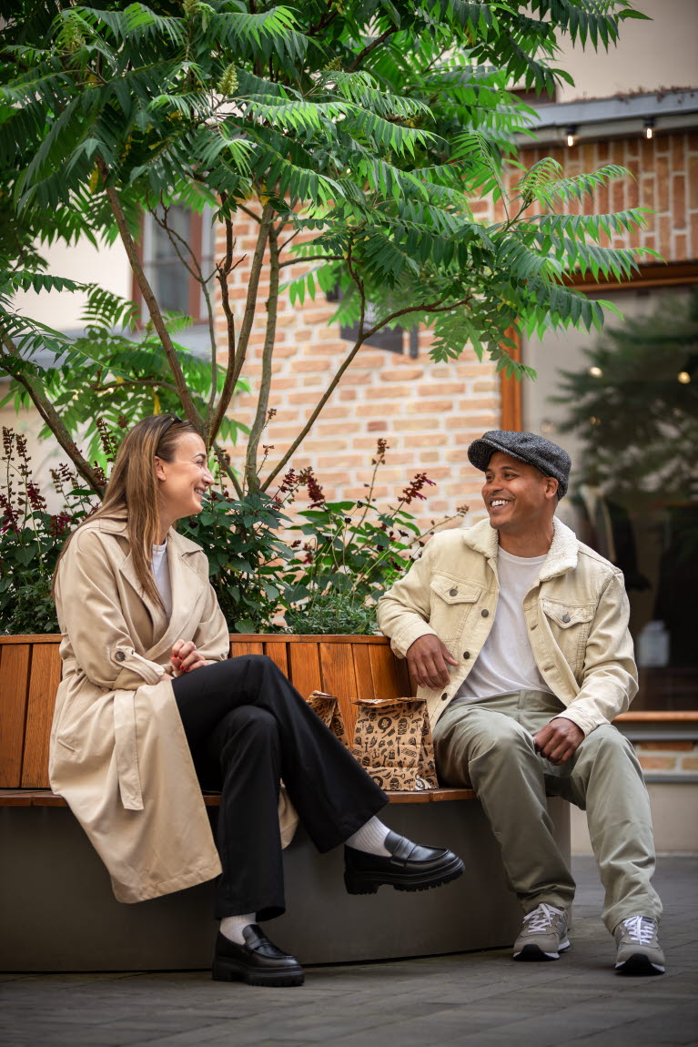 Två personer sitter på en bänk som omger ett träd. De samtalar och skrattar.