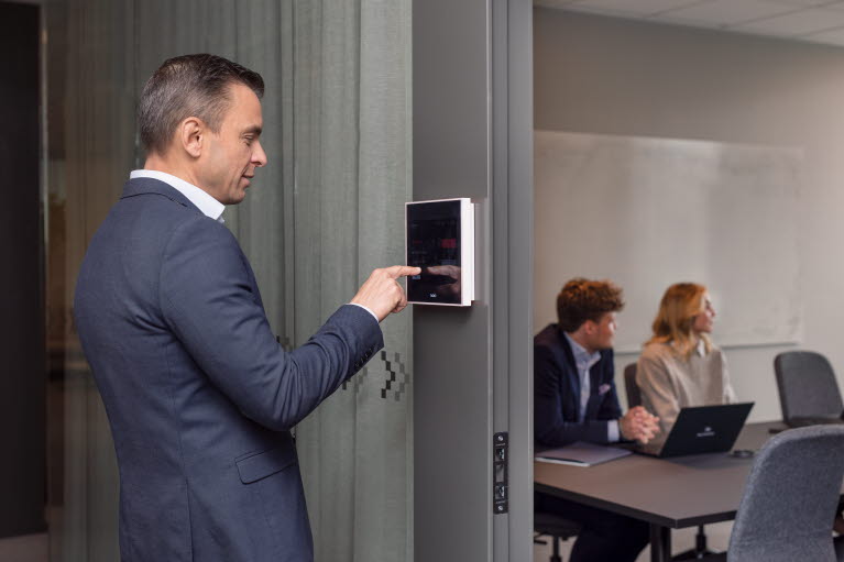 En man står och trycker på en display utanför ett konferensrum.