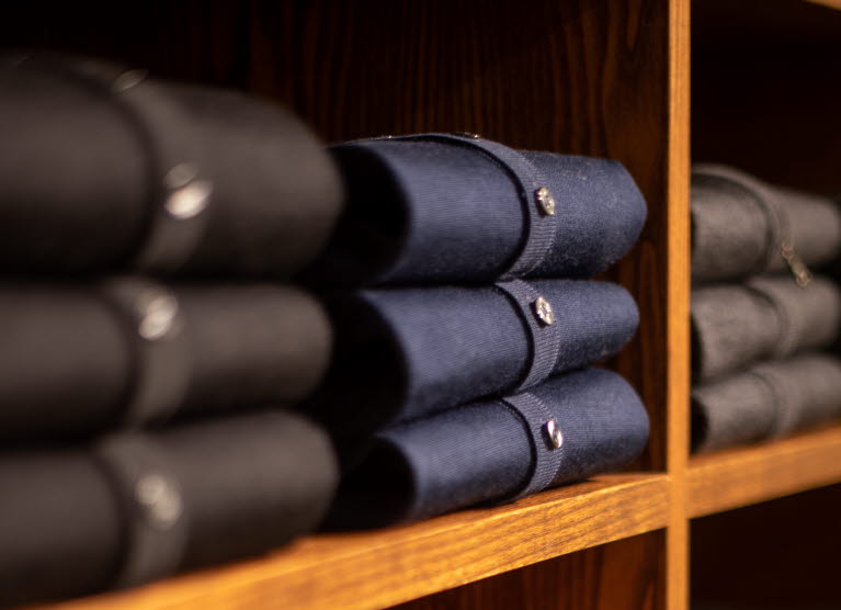 Vikta koftor i olika färger som ligger i en hylla av trä.