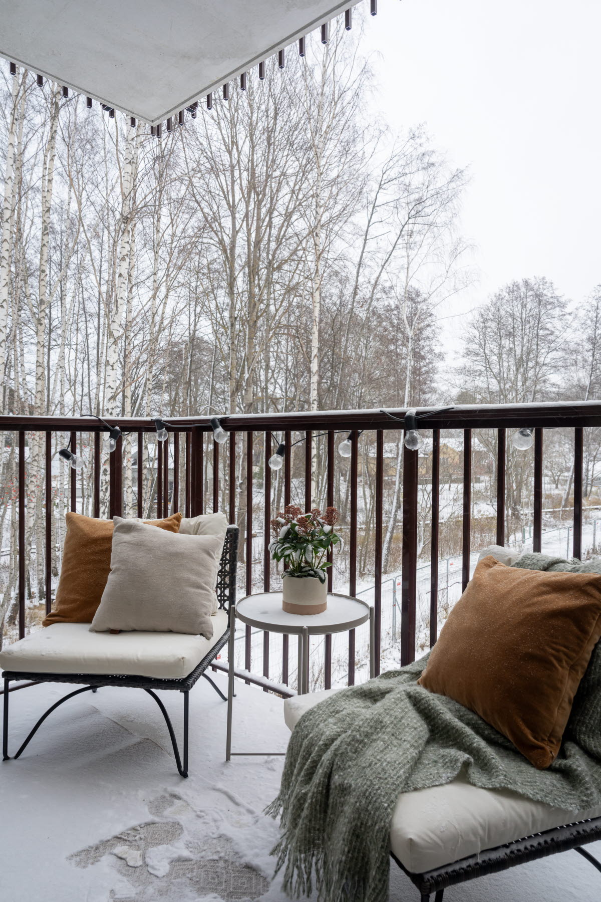 Balkongmöbler, två stolar med kuddar och filt samt ett balkongbord mellan stolarna. Snö på balkongen.