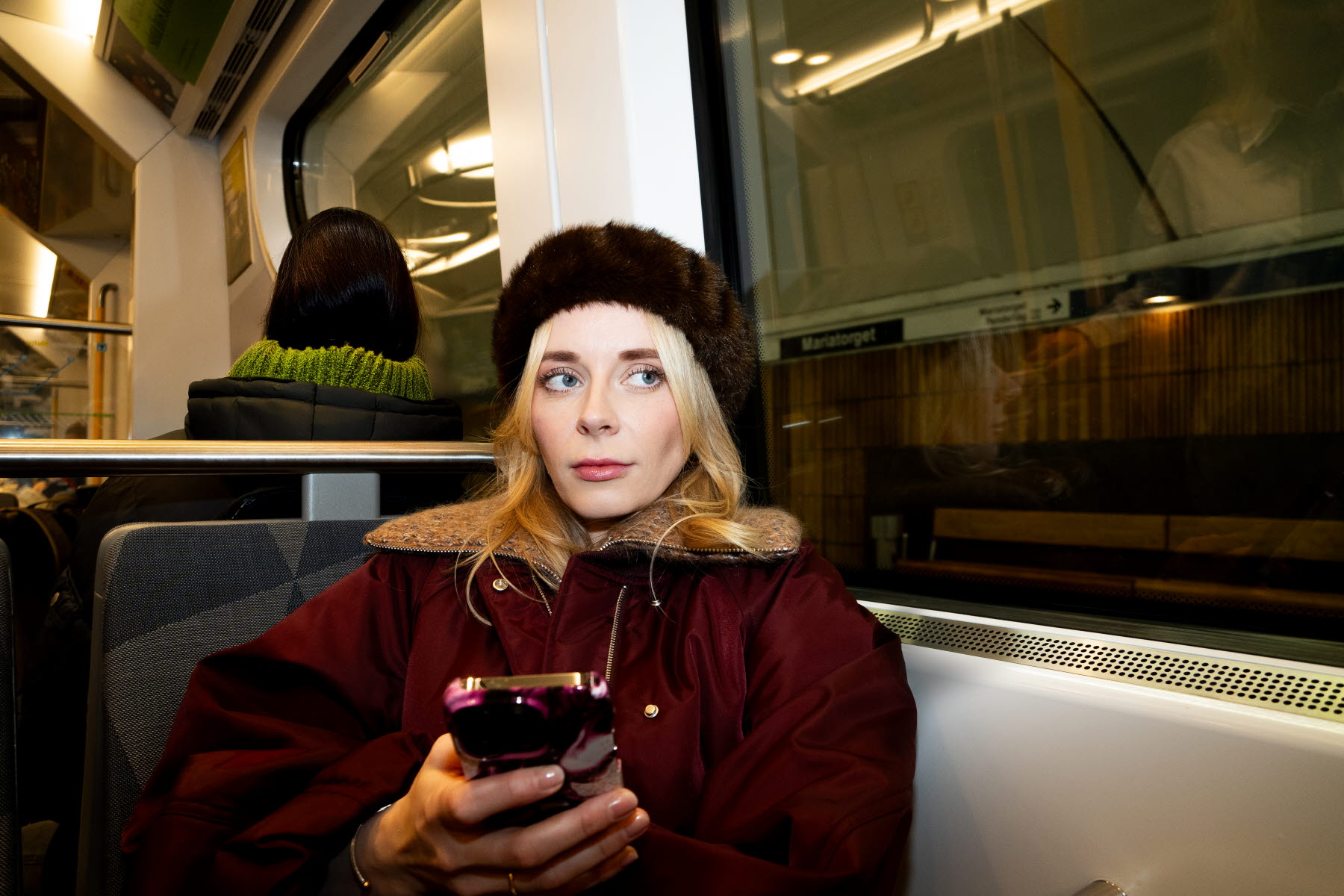 kvinna sitter i tunnelbanan med mobil i handen 