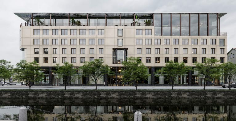 Visionsbild på fastigheten vid Stampgatan som visar huset med ny ljus fasad och ytterligare en våning hög, där nya våningen består av stora glaspratier.